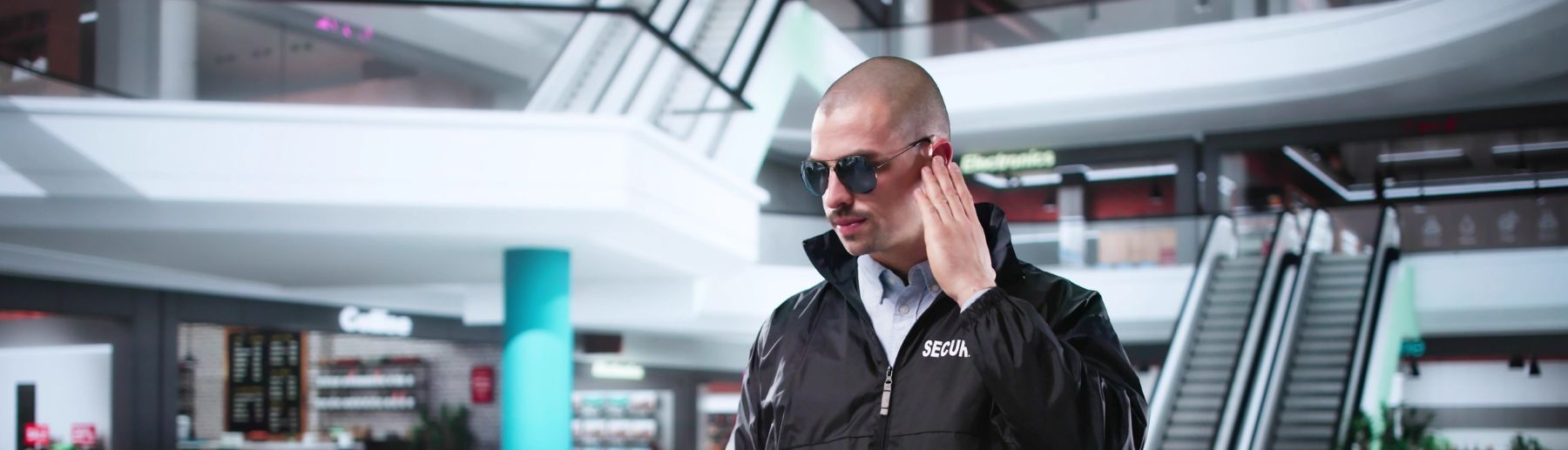A security guard wearing sunglasses and a black jacket with 
